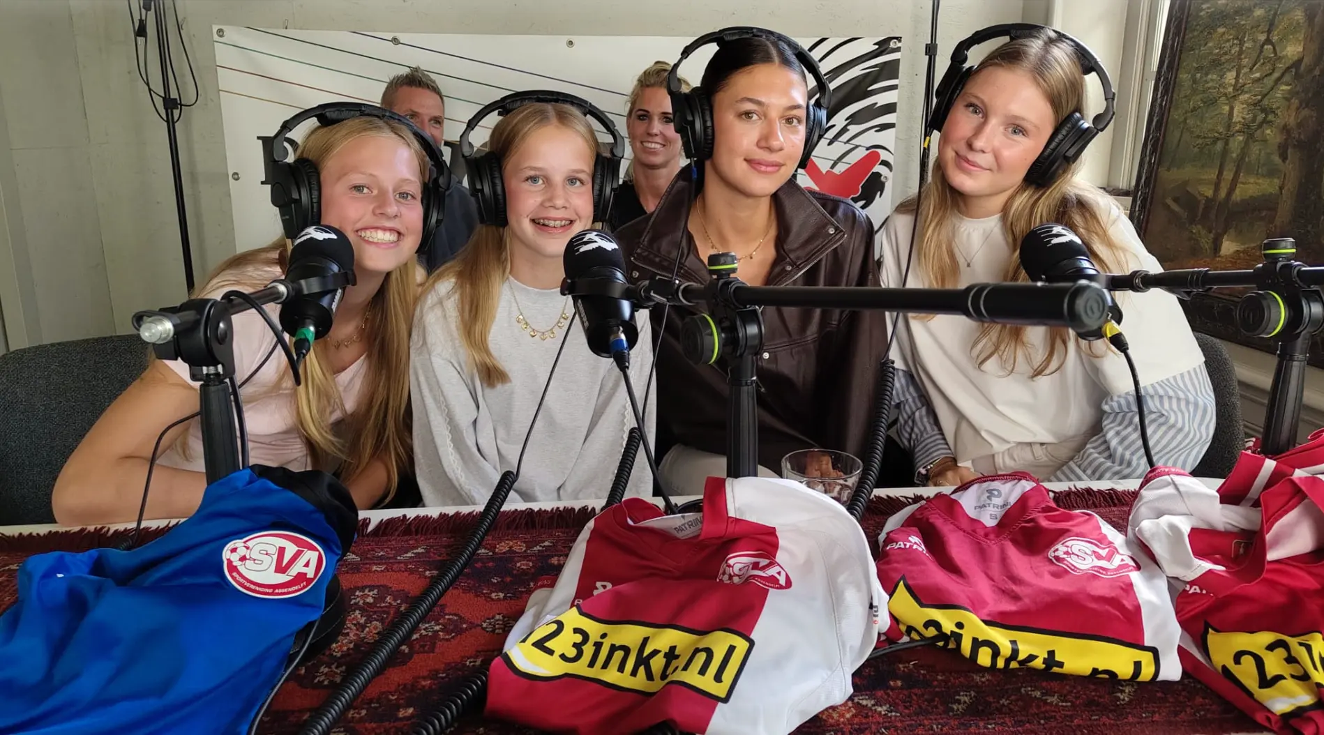 De meiden en leiders van MO15 en MO17 in de studio van Podcast De Orkaan, met koptelefoons en microfoons